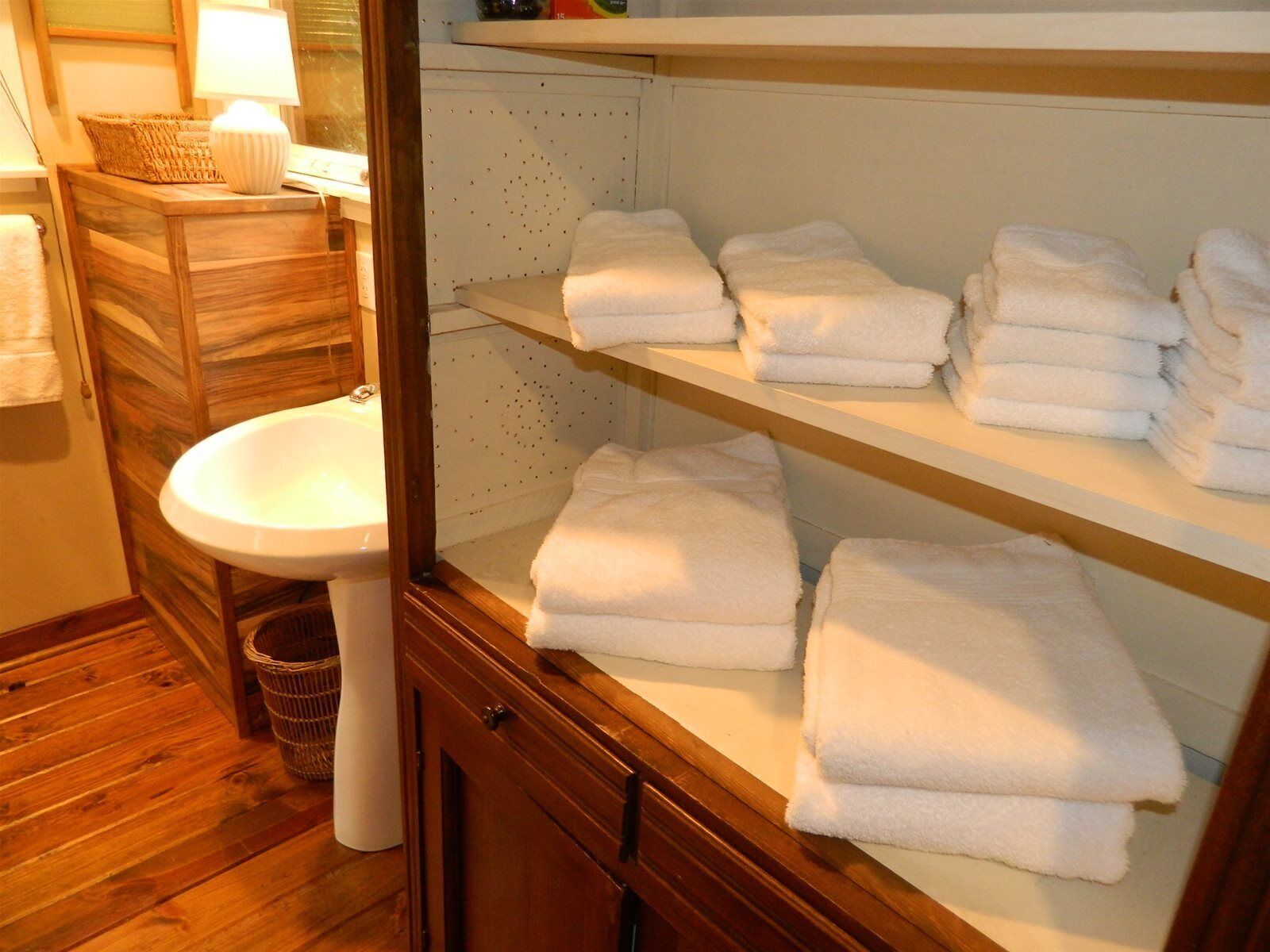 A bathroom with a wooden vanity, a white sink, and shelves holding folded towels.