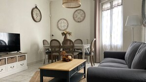 Ein Wohnzimmer mit Fernseher, Sofa, Couchtisch, Esstisch, Stühlen, dekorativen Tellern und einer Pendelleuchte.