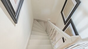 Eine weiße Treppe mit weißem Geländer, gerahmte Kunstwerke an den Wänden und eine weiße Decke.