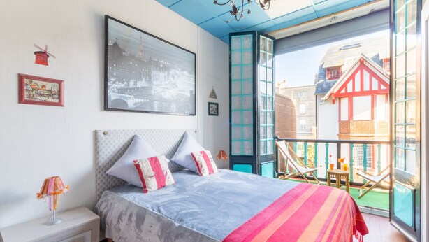 Een slaapkamer met een bed, nachtkastje en een raam met uitzicht op een balkon.