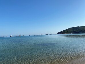 A calm sea with several sailboats anchored near a coastline with a hill.