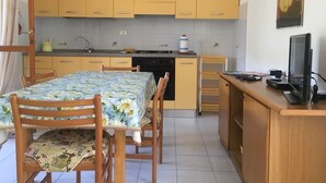 Eine kleine Küche mit gelben Schränken, einem Esstisch mit Blumenmuster und einem Fernseher auf einem Holzgestell.