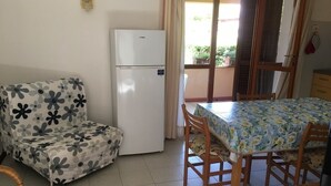 Ein Zimmer mit einer Sitzecke, einem Esstisch, einem Kühlschrank und Blick durch ein Fenster.