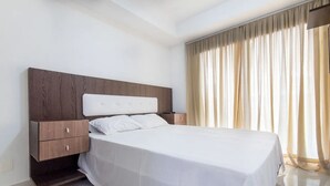 Une chambre d’hôtel moderne avec un grand lit, une tête de lit en bois et une table de chevet dotée de tiroirs.