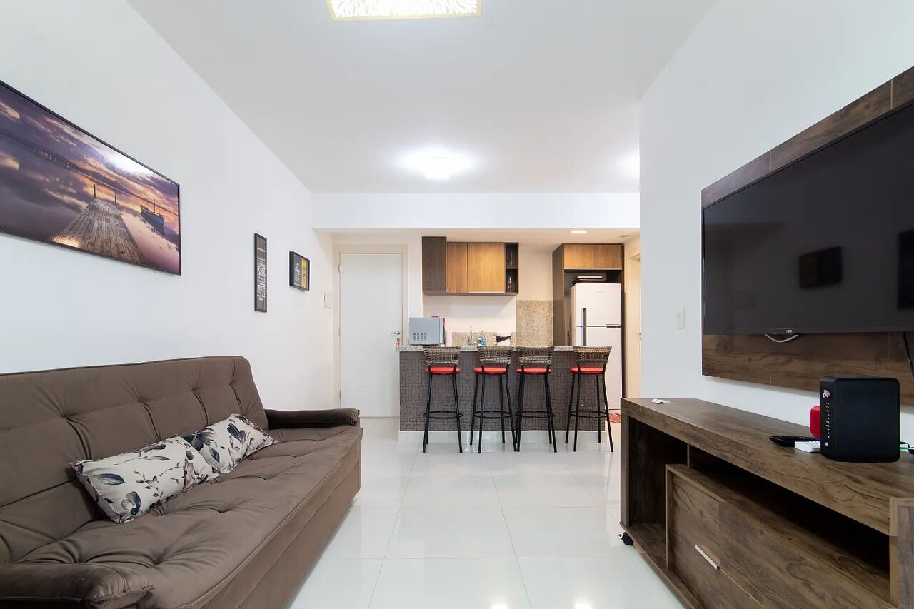 Una sala de estar moderna con un sofá marrón, un televisor de pantalla plana y una zona de cocina con un juego de taburetes de bar.