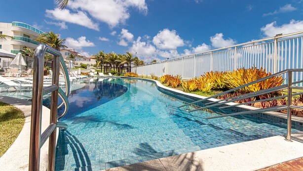 Une piscine d’un bleu éclatant, à bords incurvés, entourée de palmiers et de plantes tropicales.