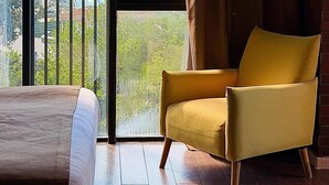 A room with a bed, a yellow armchair, and a large window with a view of a cityscape and mountains. - Bricks Hotel (Tbilisi)