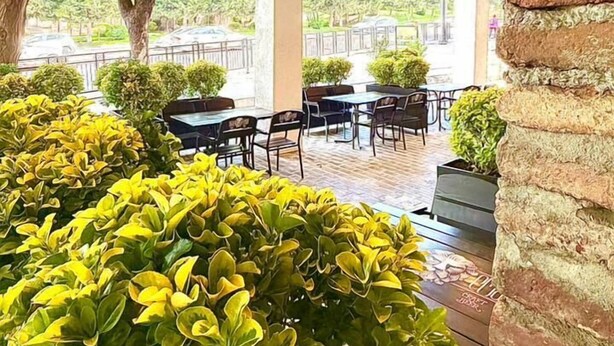 An outdoor seating area with tables and chairs, surrounded by greenery and a brick wall. - Bricks Hotel (Tbilisi)
