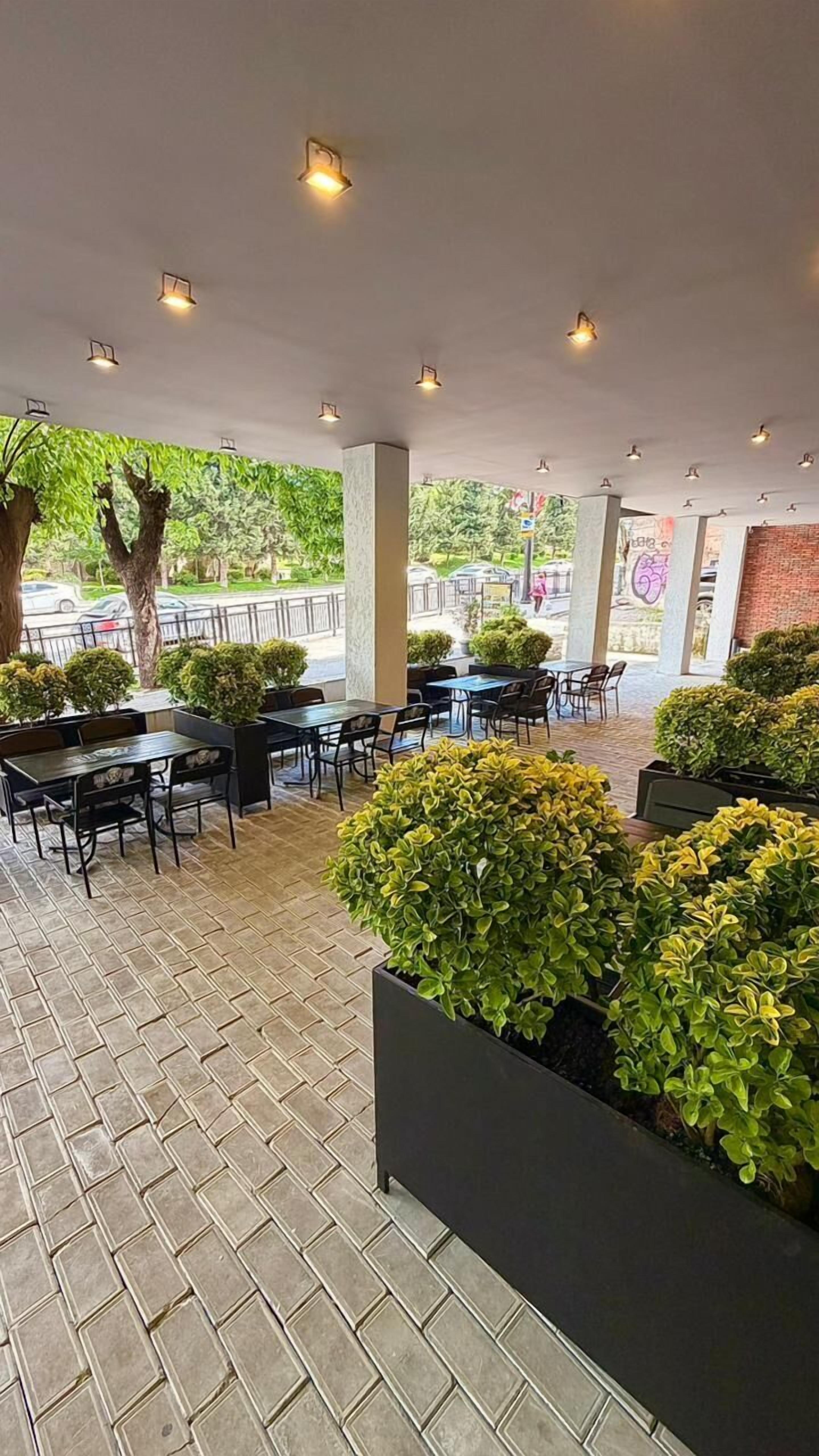 An outdoor cafe area with tables and chairs, potted plants, and a view of the street.