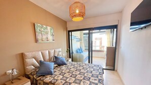 A bedroom with a bed, a nightstand, a painting, and a view through a sliding door to an outdoor balcony.