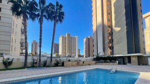 A swimming pool with a geometric tile pattern, surrounded by tall residential buildings and palm trees.