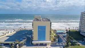 Een hotel met een groot blauw bord, een parkeerplaats en uitzicht op zee.