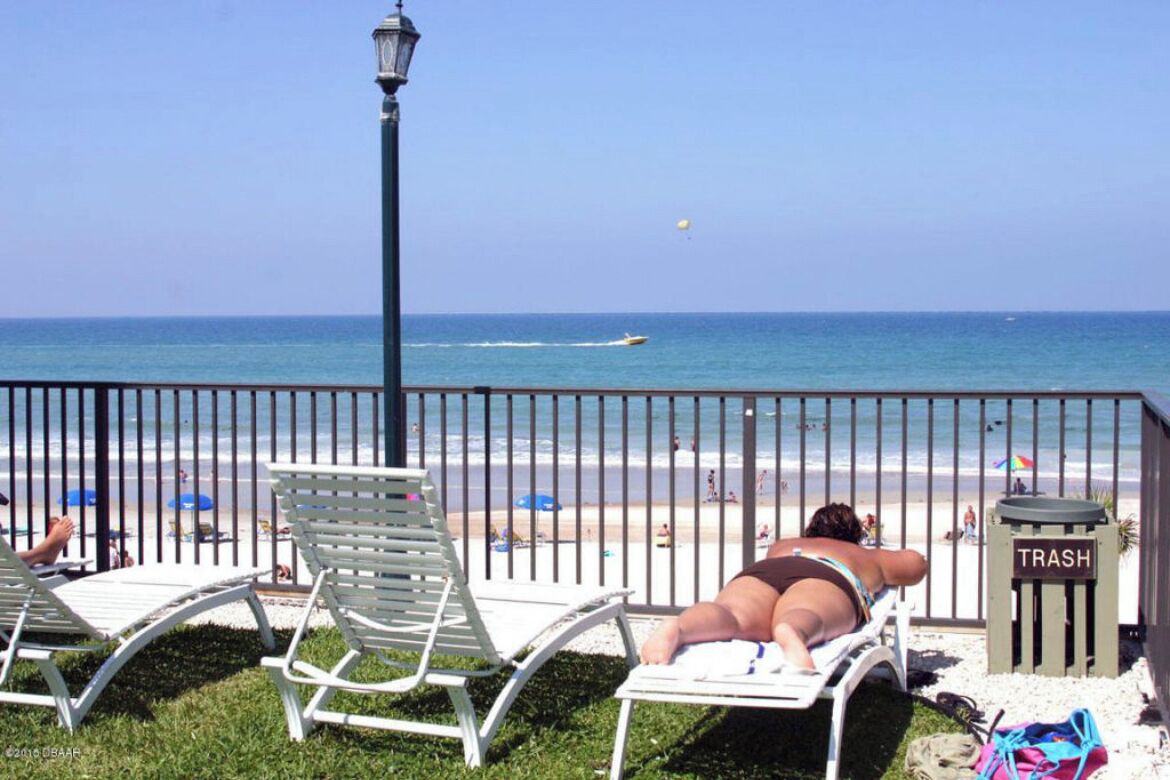 Vista da praia com cadeiras de lounge, um cesto de lixo e ampla visão do oceano.