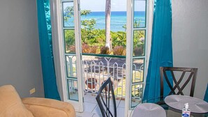 A room with a view of the ocean through a glass door, a chair, and a small table. - Malibu ocean View Studio (Montego Bay)