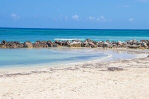 Ein Strand mit klarem türkisblauem Wasser, einer felsigen Küstenlinie und einem Sandstrand.