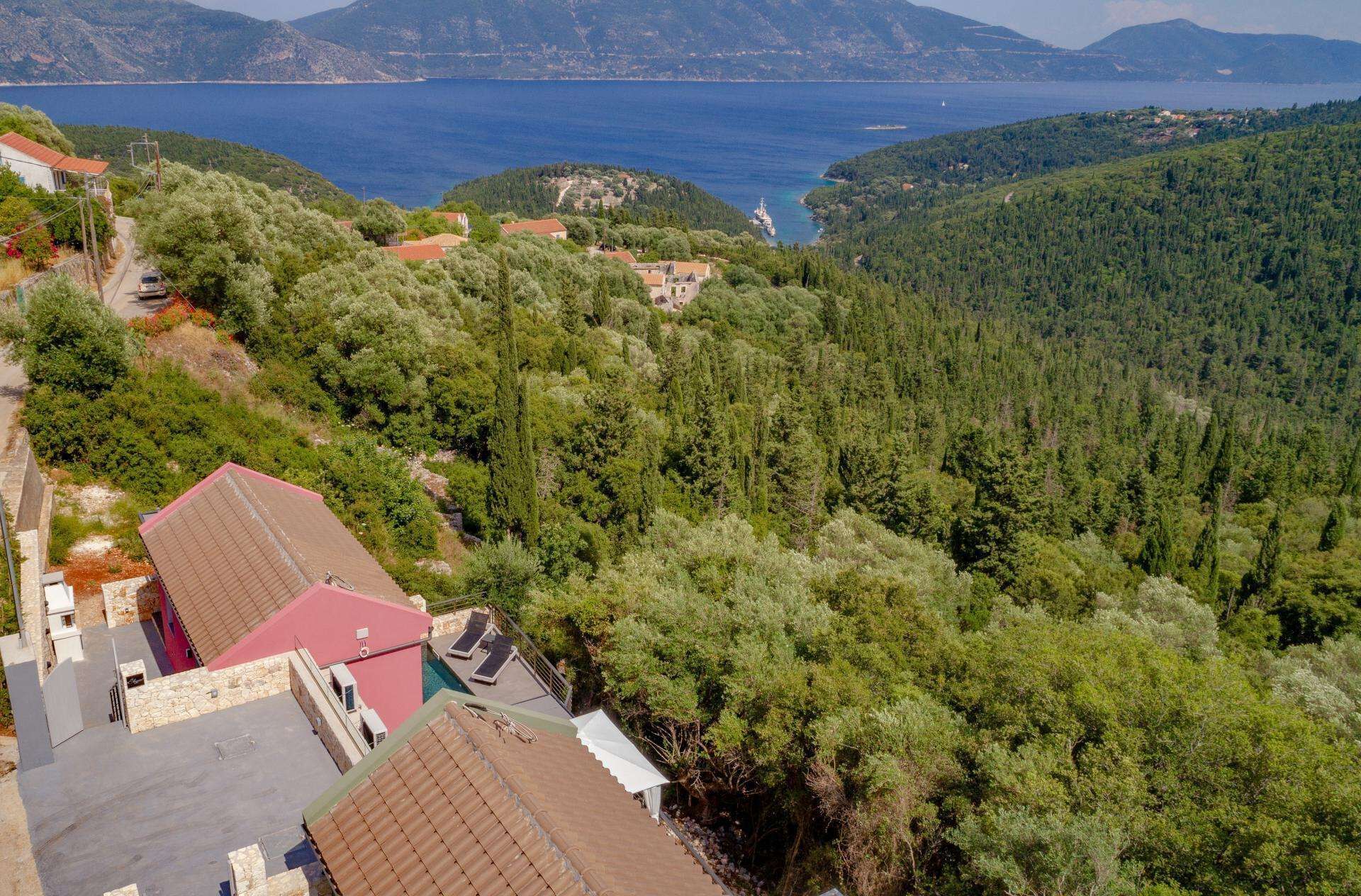 A coastal view with a house, a swimming pool, and a forested hillside.