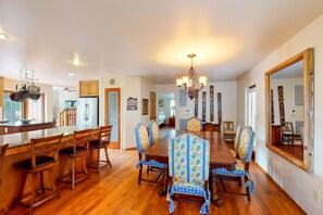A spacious dining room with a long wooden table and matching chairs, a chandelier, and a large mirror on the wall.