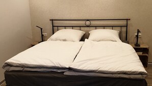 A double bed with a metal frame, white bedding, and a small bedside table with a lamp. - Ferienwohnung "Gast4" (Weikersheim)