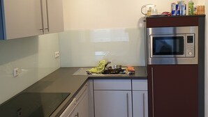 A modern kitchen with white cabinets, a black countertop, and a built-in microwave. - Ferienwohnung "Gast4" (Weikersheim)