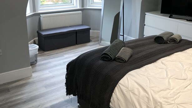 Une chambre à coucher moderne avec un lit, un banc, une télévision et une grande fenêtre.