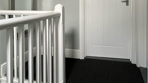 Un couloir avec une porte blanche et une rambarde blanche.