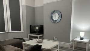 Un salon moderne avec un téléviseur à écran plat, un miroir rond, une petite table avec une lampe et un canapé.