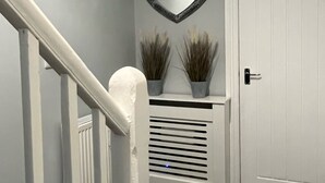 Un escalier avec des rampes blanches menant à un palier où se trouve une porte blanche et un miroir en forme de cœur fixé au mur.