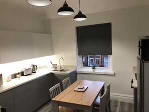 A modern kitchen with a wooden table, white cabinets, a window with a view, and pendant lighting. - Large four bedroom home in Bournemouth 
 (bournemouth)