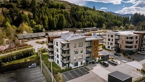 Un moderno complejo de apartamentos con varios edificios, plazas de aparcamiento y un área boscosa circundante.