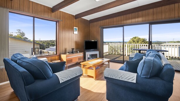Ein großzügiges Wohnzimmer mit Holzwandverkleidung, großen Fenstern und einem Balkon mit Aussicht.