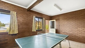 Ein Zimmer mit Tischtennisplatte, Backsteinwänden, einer Tür und fensterbepfungen Vorhängen.