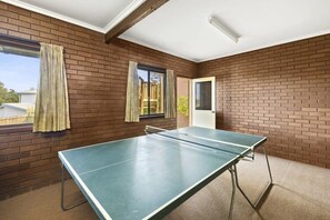 Une pièce avec une table de ping-pong, des murs en briques, une porte et des fenêtres avec des rideaux.