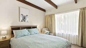 Ein Schlafzimmer mit einem Bett, einem Nachttisch, einem Sessel, einem Fenster mit Vorhängen und einem Wandbild.