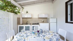 Uma cozinha compacta com fogão a gás, pia e armários brancos. Há uma mesa com toalha estampada e duas cadeiras brancas.