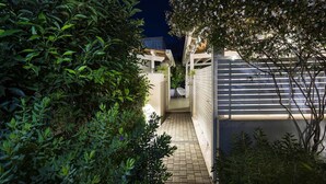 A narrow pathway leading to a gated entrance with a chair and a potted plant.
