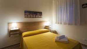 A hotel room with a bed, a bedside lamp, a painting on the wall, and a window with curtains.