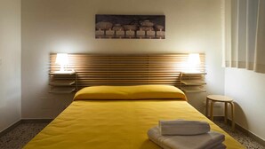 A hotel room with a bed, two bedside lamps, a painting on the wall, and a small table.