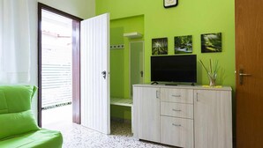 Habitació amb una paret verda, un armari de fusta amb un televisor de pantalla plana, una cadira verda i una porta que dona a un balcó.