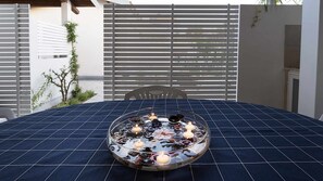 Ein runder Tisch mit dunkelblauer Tischdecke, einer Glasvase als Mittelstück mit Kerzen und einem weißen Stuhl.