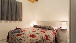 A bedroom with a bed, two bedside lamps, a nightstand, a window with curtains, and a wooden ceiling.