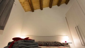 A bedroom with a wooden ceiling, a bed with floral bedding, a bedside table with a lamp, and a window with curtains. - (B67) Cozy house with veranda 150 mt from the sea (Marina Di Modica)