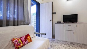 A room with a white sofa, a colorful pillow, a TV on a cabinet, and a door leading outside. - (B67) Cozy house with veranda 150 mt from the sea (Marina Di Modica)
