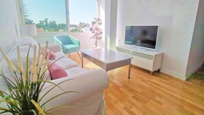 Ein modernes Wohnzimmer mit einem weißen Sofa, einem blauen Sessel, einem Couchtisch und einem Flachbildfernseher auf einem weißen Lowboard.