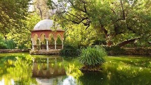 Ein friedlicher Garten mit einem Pavillon an einem Teich, umgeben von üppigem Grün.