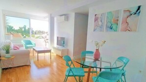 Ein modernes Wohnzimmer mit einem Glastisch, türkisfarbenen Sesseln, einem weißen Sofa und einem Fernseher.