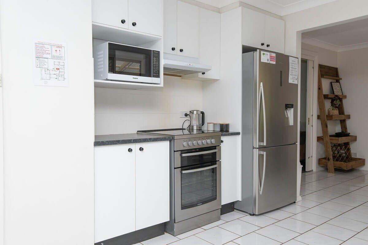 A modern kitchen with white cabinets, a built-in microwave, a stainless steel refrigerator, and an oven.