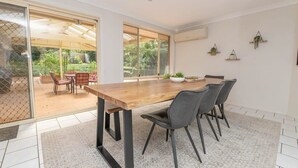 Zona pranzo con tavolo in legno, sedie nere e un'ampia finestra con vista su un giardino.