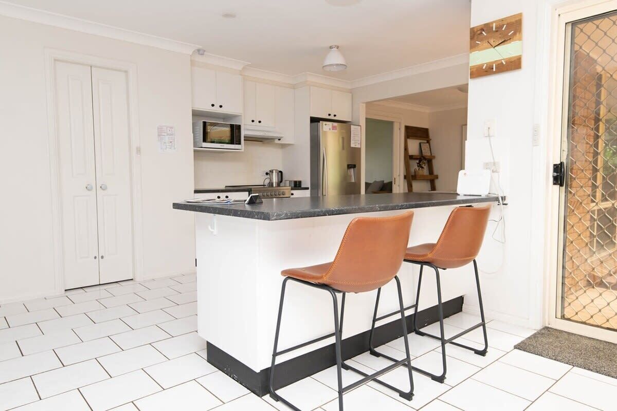 A modern kitchen with white cabinets, a black countertop, and two brown bar stools.