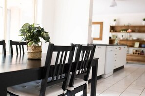 A modern kitchen with white cabinets, a black countertop, and a dining area with black chairs and a woven plant basket. - The Valerie Gardens. Five bedrooms. Orange. (Orange)