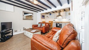 A living room with a brown leather sofa, a TV, and a wooden coffee table. There is a kitchen visible in the background. - 5 Ivy Yard (Whitby)